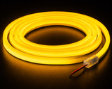 A coiled Color IP44/IP66 Neon Flexible LED Light Line (24V) ~ Flex Ultra Slim Series glows bright yellow against a dark background, with one end showing exposed wires inside a clear plastic casing.