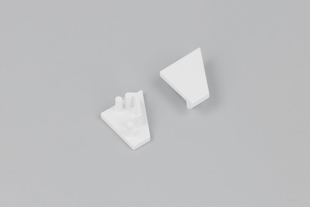 Two small, white, triangular plastic components—each an End Cap for the Corner10.v2 Profile lighting fixture—are displayed on a plain gray background. One end cap is flat, while the other features three short cylindrical pegs on its surface.