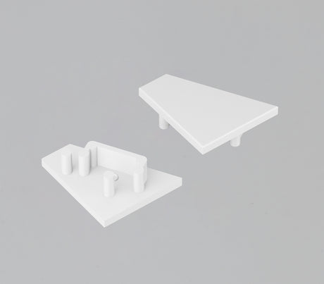 Two white, triangular End Caps for the Corner12.v2 Profile are displayed on a gray background. One has a smooth surface with two pegs below, and the other features three pegs plus a rectangular slot for a lighting fixture.