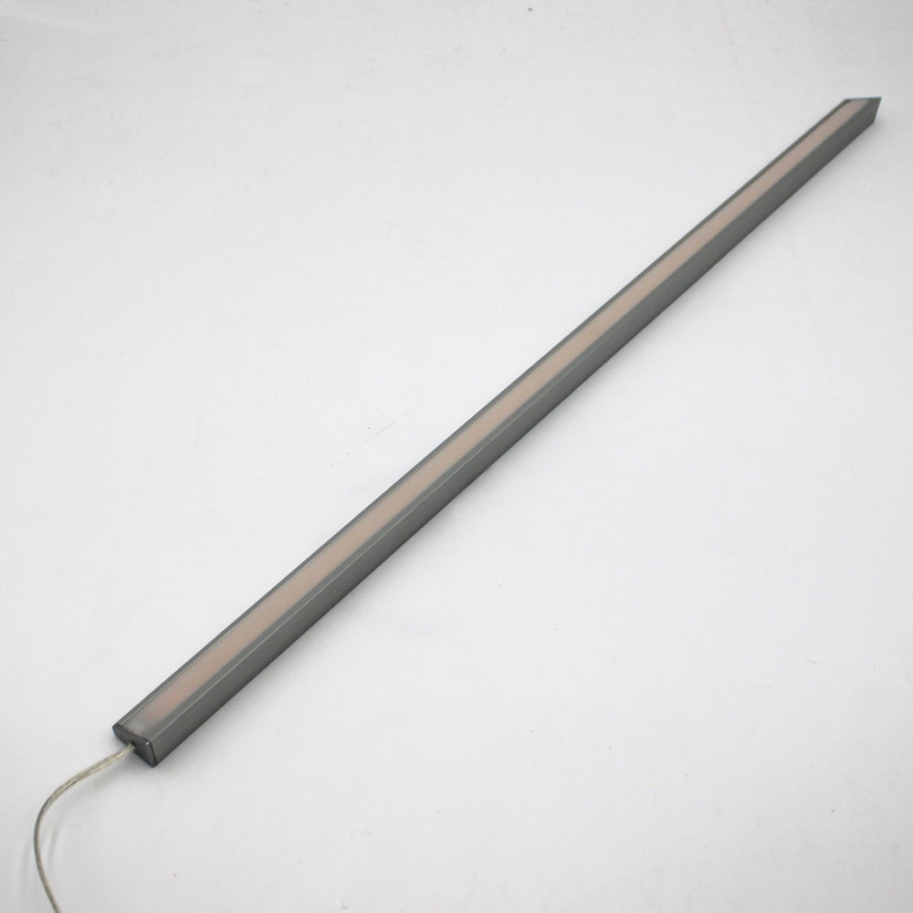 The White Universal Surface-mount LED Corner Lighting Fixture (24V) ~ Corner14 Series, featuring a slim rectangular design with a gray frame and frosted cover, lies diagonally on a white surface with its power cord extending from one end.