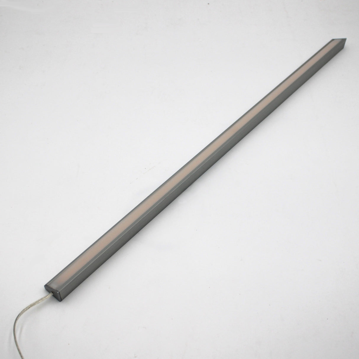The White Universal Surface-mount LED Corner Lighting Fixture (24V) ~ Corner14 Series, featuring a slim rectangular design with a gray frame and frosted cover, lies diagonally on a white surface with its power cord extending from one end.