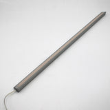 The White Universal Surface-mount LED Corner Lighting Fixture (24V) ~ Corner14 Series, featuring a slim rectangular design with a gray frame and frosted cover, lies diagonally on a white surface with its power cord extending from one end.