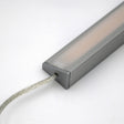 A close-up of the White Universal Surface-mount LED Corner Lighting Fixture (24V) ~ Corner14 Series, featuring a frosted cover and transparent power cord, ideal for under-cabinet lighting, shown against a plain white background.