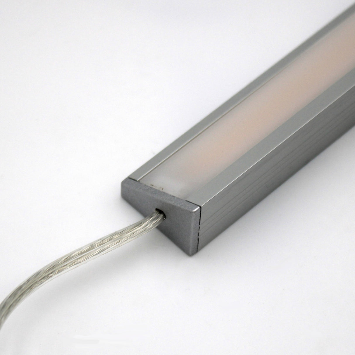 A close-up of the White Universal Surface-mount LED Corner Lighting Fixture (24V) ~ Corner14 Series, featuring a frosted cover and transparent power cord, ideal for under-cabinet lighting, shown against a plain white background.