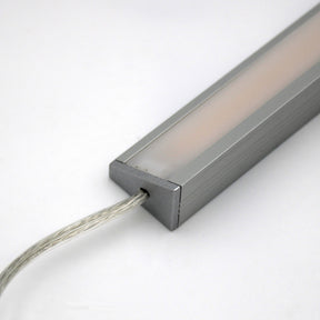 A close-up of the White Universal Surface-mount LED Corner Lighting Fixture (24V) ~ Corner14 Series, featuring a frosted cover and transparent power cord, ideal for under-cabinet lighting, shown against a plain white background.