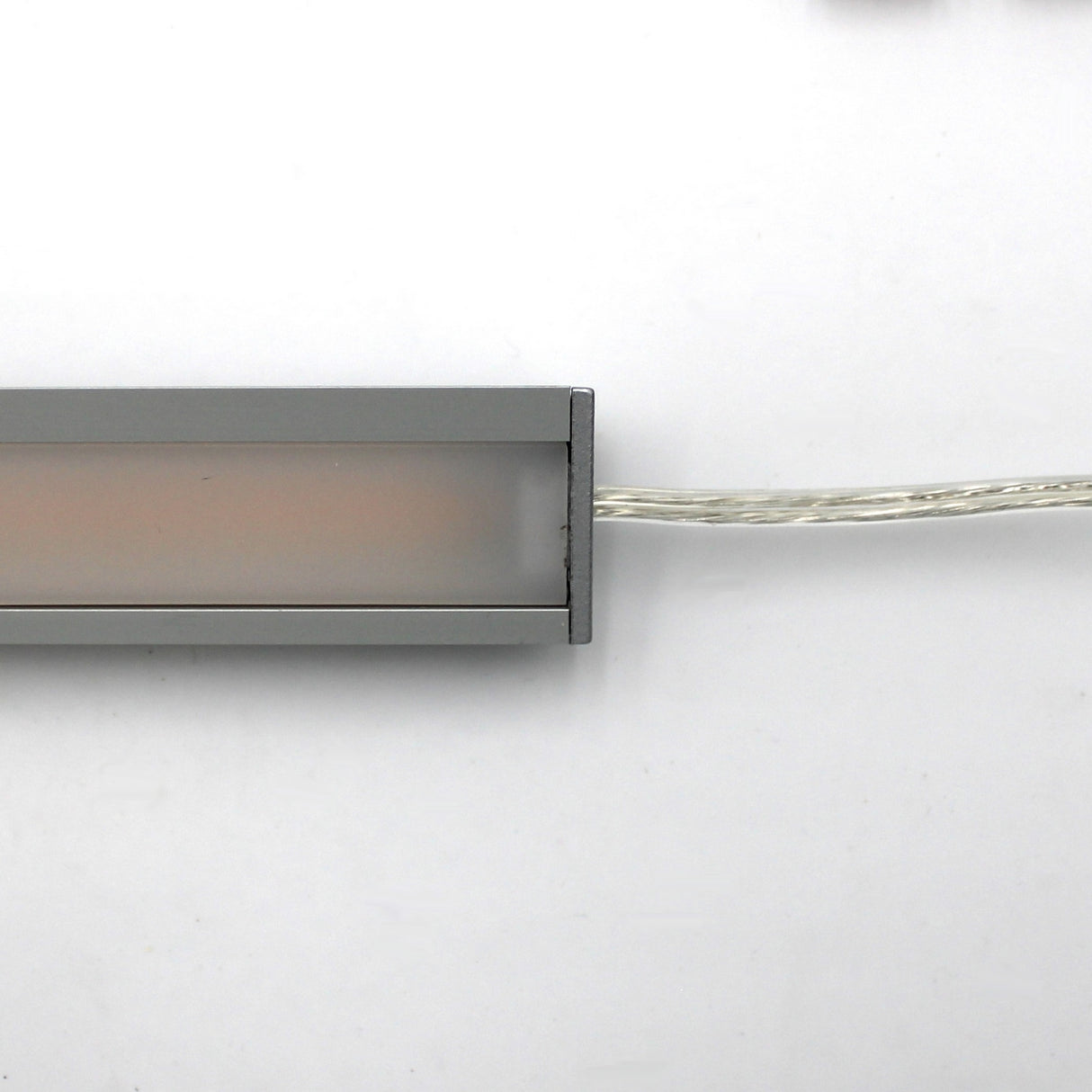 A close-up of the White Universal Surface-mount LED Corner Lighting Fixture (24V) ~ Corner14 Series, rectangular with a frosted cover, placed horizontally on a white background. Perfect for under cabinet lighting with a power cord on the right.