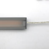 A close-up of the White Universal Surface-mount LED Corner Lighting Fixture (24V) ~ Corner14 Series, rectangular with a frosted cover, placed horizontally on a white background. Perfect for under cabinet lighting with a power cord on the right.