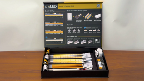 An EnoLED LED Strip Sample Box is open on a table, displaying multiple yellow LED strips, connectors, power adapters, and an instruction guide inside the box lid.