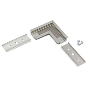 The 90 Degree Corner Connector for Groove14 Profile, featuring an L-shaped silver bracket and two straight mounting clips with screw holes, is displayed on a white background; two screws are positioned next to the L-shaped bracket.