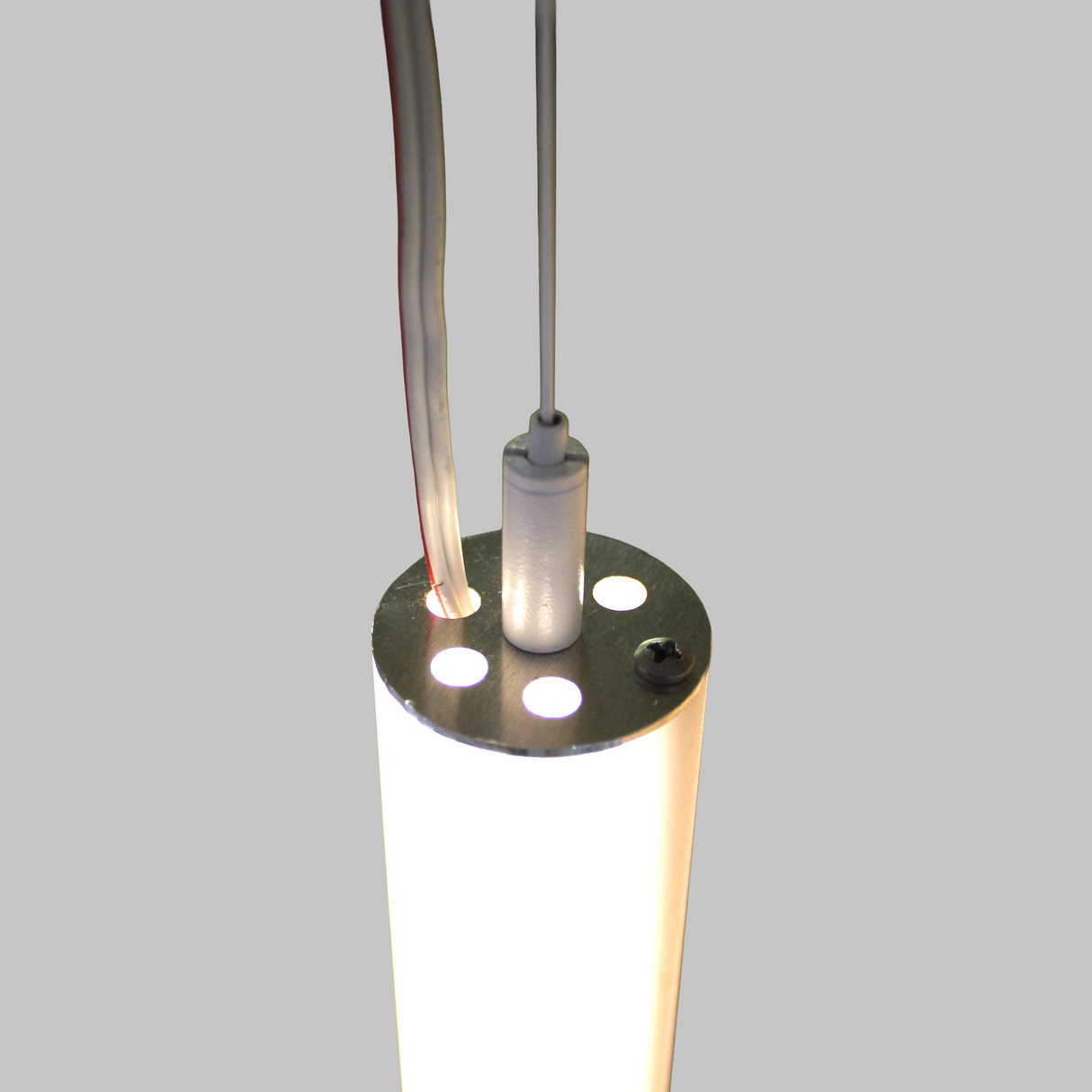 A close-up of the Aluminum End Cap for Sierra38 Profile, attached to a cylindrical LED fixture with a metal top, emitting bright white light. Two wires, one clear and one white, extend from the top against a plain gray background.