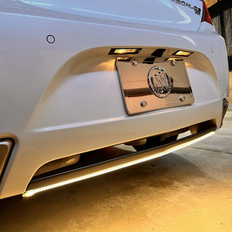 A white car’s rear bumper featuring a White IP68 Waterproof LED Strip (12V) ~ White Iris Series installed along the bottom edge.