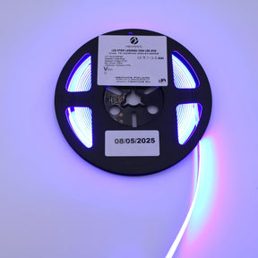 The 450nm COB IP20 LED Strip For Medical Lighting (5V) ~ Aloe Vera Series emits vibrant blue light ideal for phototherapy, features a technical label and a date sticker (08/05/2025), and is shown partially unrolled and brightly glowing.