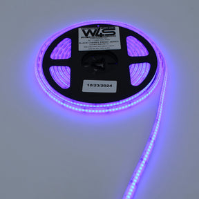 A reel of WS RGB COB IP67 LED Strip (24V) ~ Black Cherry Frost Series emits a purple glow. The labeled reel, dated 10/23/2024, sits on a white surface with the strip extending outward.