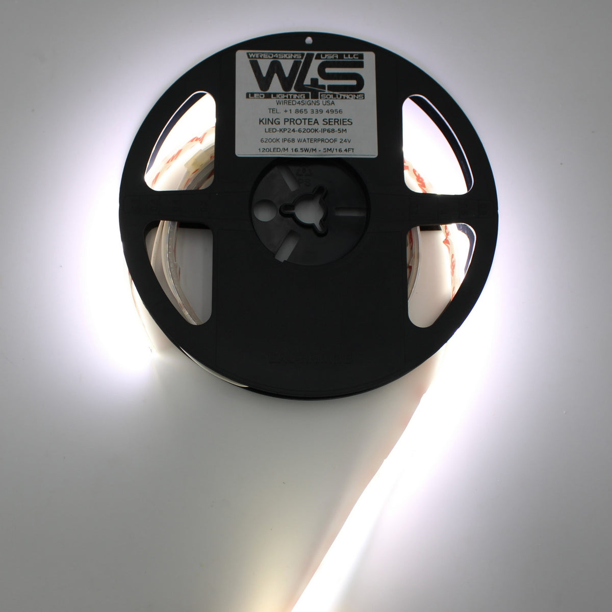 A reel of White High Output IP68 Waterproof LED Strip (24V) from the King Protea Series is partially unspooled, glowing brightly and illuminating the area around it.