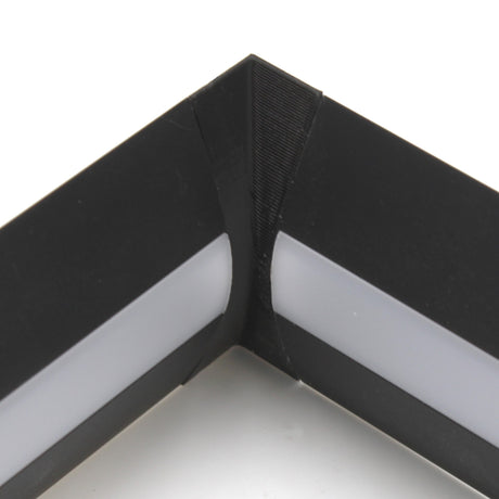 Close-up of a black Alu-Flat profile picture frame corner with a white inner edge, highlighting the precise joint formed by the Plastic Corner Connector for Alu-Flat Profile at a right angle.