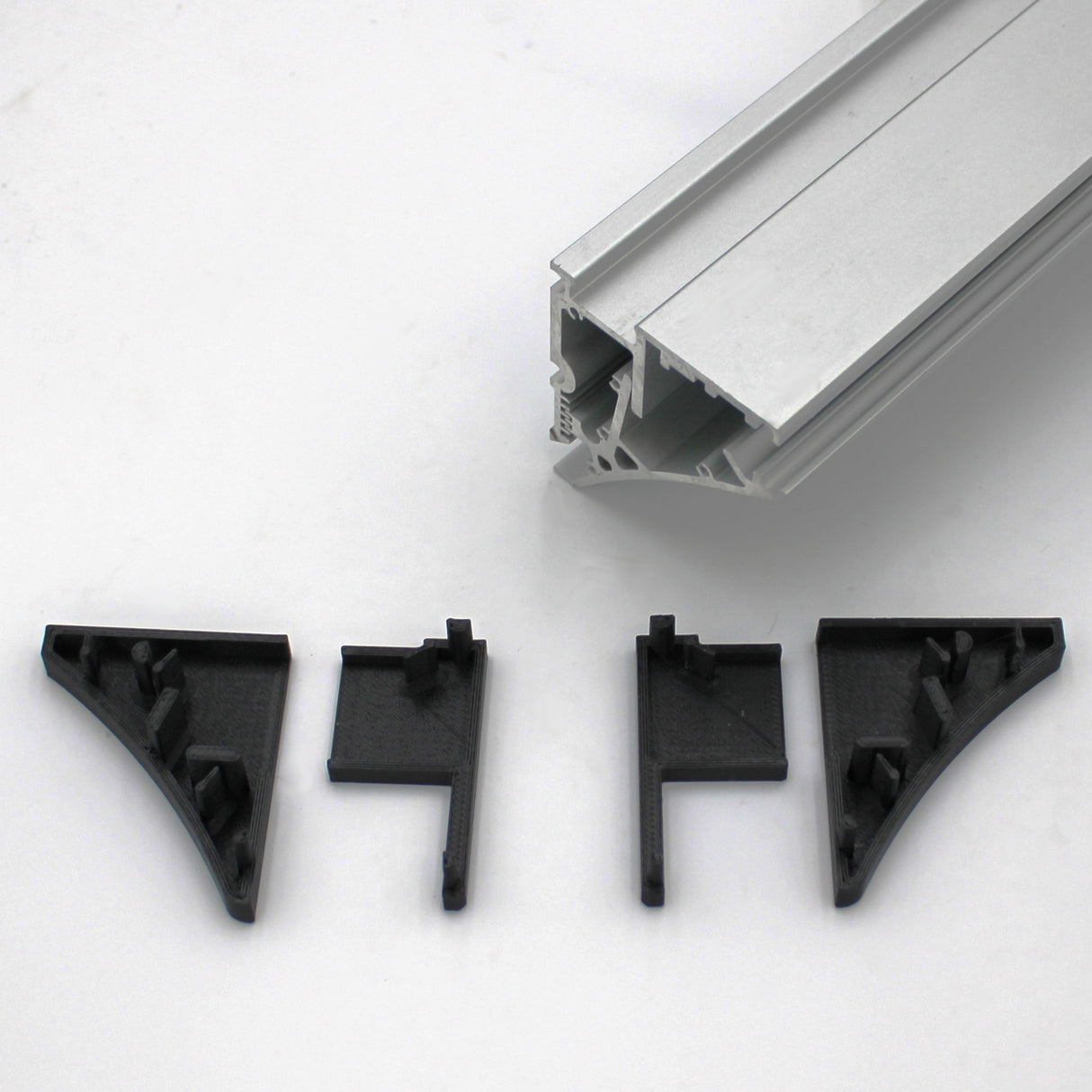 A silver Pula P10 edge-lit shelf profile sits above three black plastic corner brackets and an End Cap for Pula P10 Profile, all arranged on a white background. The brackets and end cap are designed to fit the extrusion.