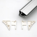 Four white End Caps for Pula P10 Profile are arranged below a Pula P10 edge-lit shelf profile rail with grooves, all displayed on a plain white background. The end caps are designed to fit and support the rail’s corners.