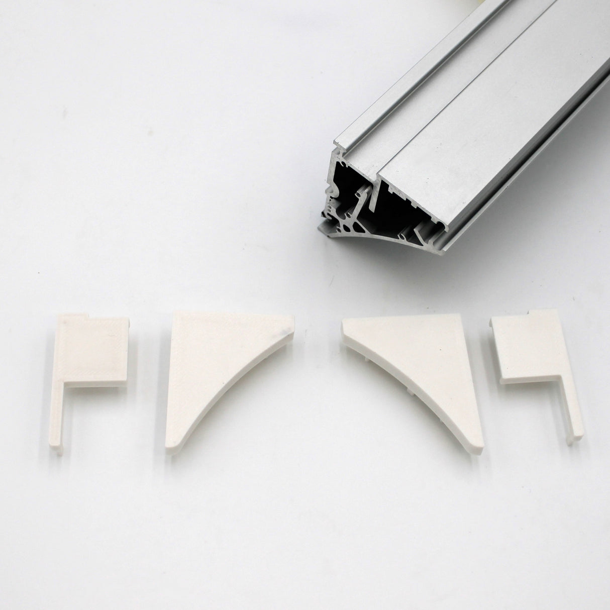 A silver Pula P10 edge-lit shelf profile extrusion bar with a hollow design is shown above four white End Caps for the Pula P10 Profile, each made of PETG plastic in different shapes, all on a white background.