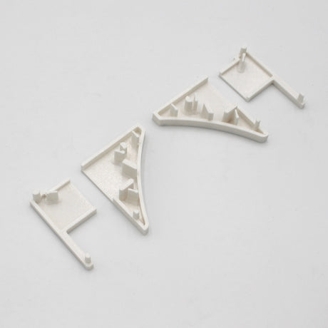 Three off-white PETG plastic End Caps for the Pula P10 Profile, featuring angular and rectangular shapes with raised pegs and flat bases, are arranged on a plain light gray background.