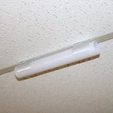 A close-up of a fluorescent light fixture mounted on a white, speckled drop ceiling tile using the Drop Ceiling T-Bar Clip for 1.5 Round Profiles for secure ceiling t-bar installation.