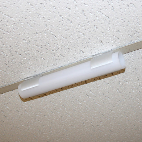 A close-up of a fluorescent light fixture mounted on a white, speckled drop ceiling tile using the Drop Ceiling T-Bar Clip for 1.5 Round Profiles for secure ceiling t-bar installation.