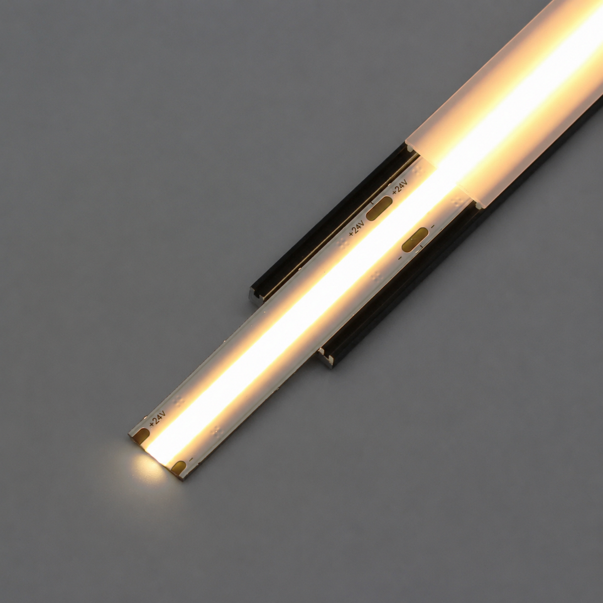 A close-up of the illuminated COB IP20 Dotless LED Strip (24V) from the UniBasic Series on a gray background, showing individual LED segments glowing with a warm white light.