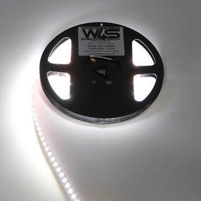 A spool of White High CRI IP20 LED Strip (24V) from the White Iris Series is partially unrolled and lit, casting a bright glow on a white surface.