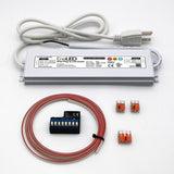 The Blebox Plug-in Power and Control Kit (24V) features a silver IP65 LED driver, attached white power cord, coiled red wire, blue terminal block, wiring accessories, and three orange connectors, all shown on a white background.