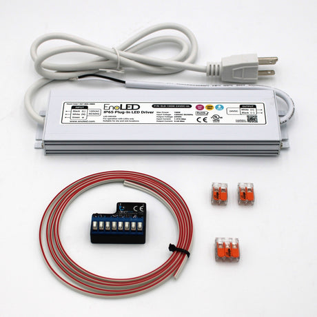 The Blebox Plug-in Power and Control Kit (24V) features a silver IP65 LED driver, attached white power cord, coiled red wire, blue terminal block, wiring accessories, and three orange connectors, all shown on a white background.