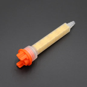 The High-Performance All-Ratio Mixer for 2-Part Methacrylate ~ Xemex F-System Snap-In features an orange cap, translucent body, and spiral yellow mixer for precise blending, shown on a dark gray surface.