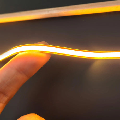 A thin, flexible yellow Ultra-Thin Flexible COB IP20 High CRI LED Strip (24V) ~ EnoLed Micro Series being held between a finger and thumb.