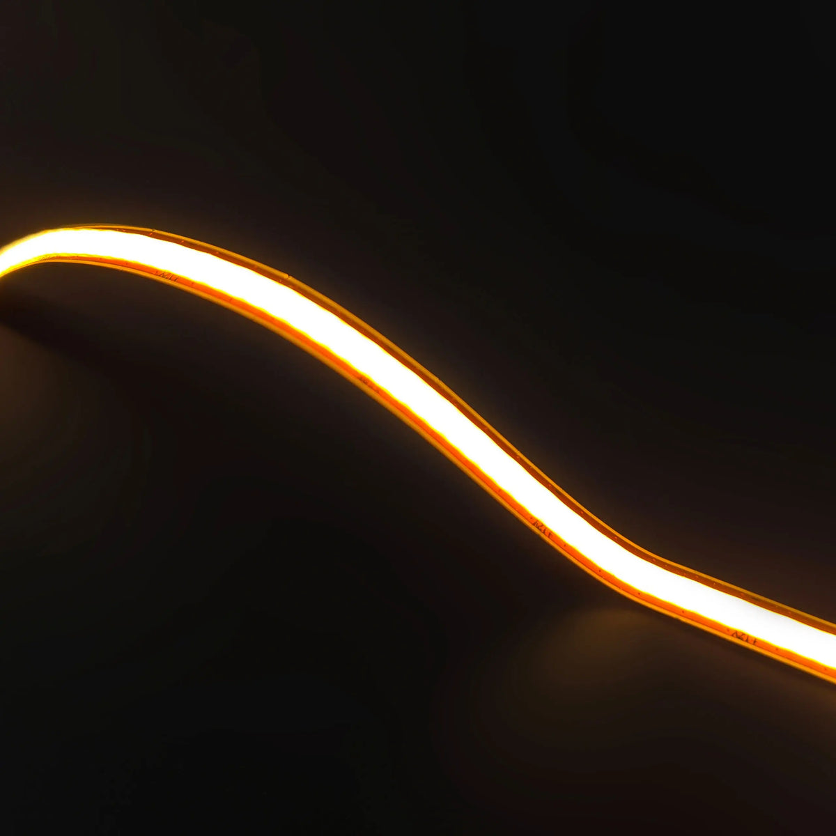An Ultra-Thin Flexible COB IP20 High CRI LED Strip (24V) ~ EnoLed Micro Series glows with warm orange light, curved into a gentle wave against a dark background.