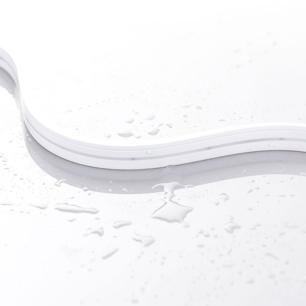 The White IP44/IP66 Neon Flexible LED Light Line (24V) ~ Flex Ultra Slim Series rests on a glossy surface with scattered water droplets, showcasing its minimal and clean design for architectural lighting applications.