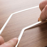 Close-up of two hands assembling a White IP44/IP66 Neon Flexible LED Light Line (24V) ~ Flex Ultra Slim Series on a wood-textured surface. The bright, architectural LED contrasts with the light brown wood grain.