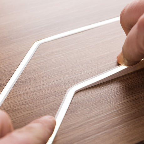 Close-up of two hands assembling a White IP44/IP66 Neon Flexible LED Light Line (24V) ~ Flex Ultra Slim Series on a wood-textured surface. The bright, architectural LED contrasts with the light brown wood grain.