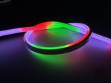 The Pixel IP44/IP66 Neon Flexible LED Light Line (24V) ~ Flex Slim Series glows in red, green, and purple, forming a loose loop on a dark surface.