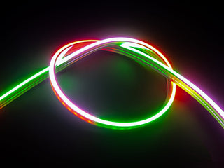 A twisted loop of the Pixel IP44/IP66 Neon Flexible LED Light Line (24V) ~ Flex Super Slim Series emits red, green, and white light against a dark background.