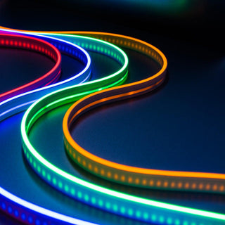 The Color IP44/IP66 Neon Flexible LED Light Line (24V) ~ Flex Ultra Slim Series glows in red, blue, green, and orange on a dark surface, creating vivid, futuristic waves with its smooth, ultra-slim neon design.