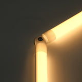 Close-up of a glowing, L-shaped LED tube light joined at the corner by the Hinge for Oslo Mini Profile, featuring an adjustable lighting hinge and a sleek diffuser tube system against a plain wall.