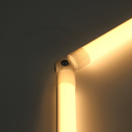 Close-up of a glowing, L-shaped LED tube light joined at the corner by the Hinge for Oslo Mini Profile, featuring an adjustable lighting hinge and a sleek diffuser tube system against a plain wall.
