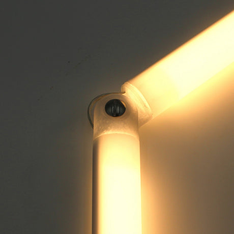 Close-up of a glowing LED light fixture with a Hinge for Oslo Mini Profile, mounted on the wall and emitting warm yellowish light. The adjustable hinge forms an angled joint, secured by a visible screw.