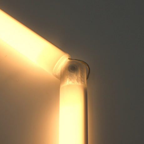 Close-up of two glowing, tube-shaped LED lights joined at a right angle by a Hinge for Oslo Mini Profile, forming part of a sleek diffuser tube system against a plain, light-colored background.