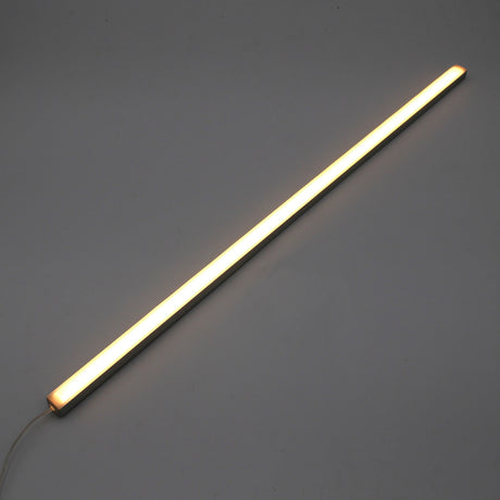 The White Universal Surface-mount Waterproof Outdoor LED Lighting Fixture (24V) ~ Roma Series emits a warm white glow as a slim, dotless LED bar shown diagonally on a plain gray background, with its power cord visible for versatile outdoor use.