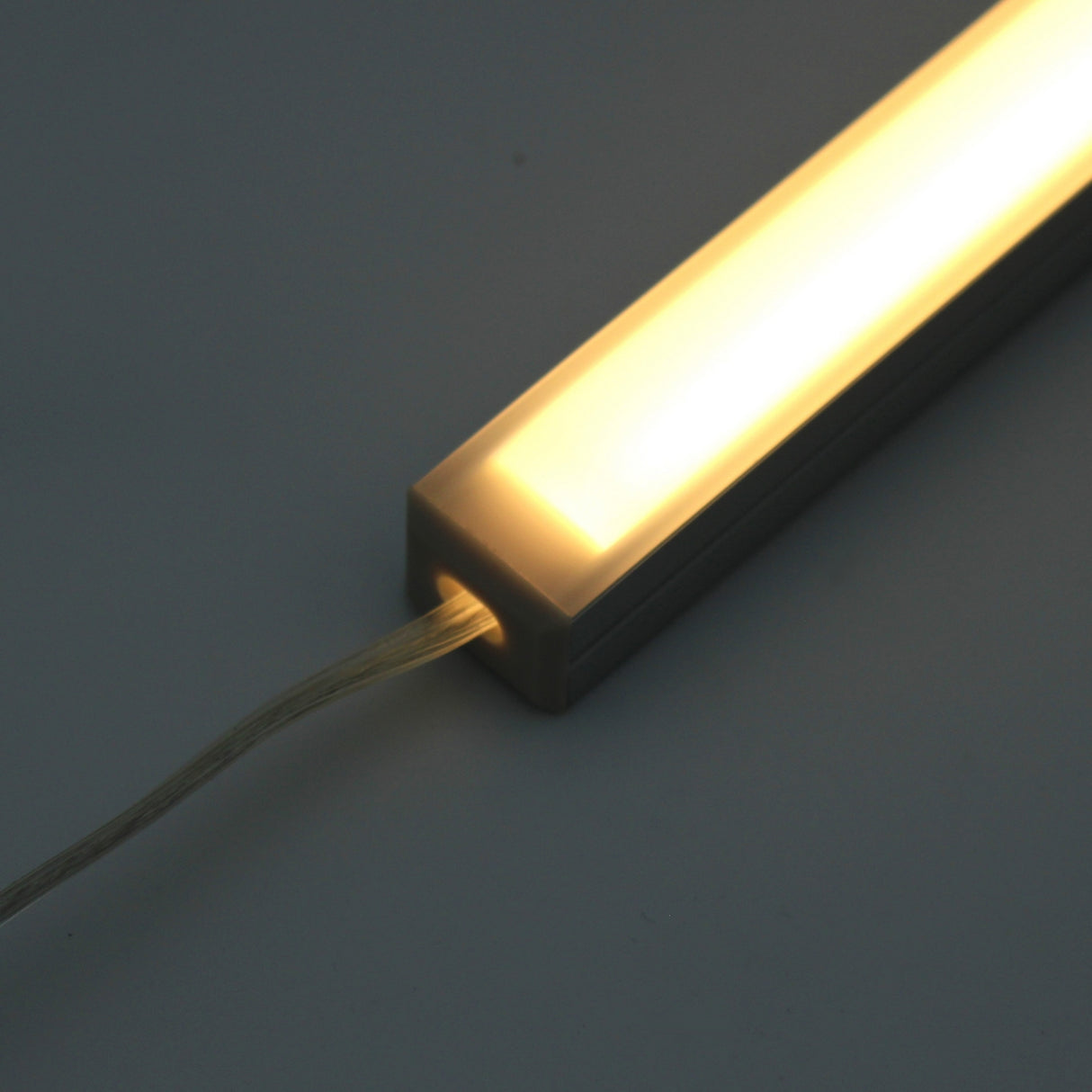 The White Universal Surface-mount Waterproof Outdoor LED Lighting Fixture (24V) ~ Roma Series features a translucent cover, dotless light, and an electrical cord at one end, shown against a plain dark background.