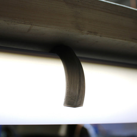 A Mounting Clip for 2.56" Round Profiles secures a fluorescent tube, shown with a crescent-shaped smudge on its surface, beneath a metal fixture.