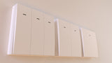 Four minimalist, wall-mounted white cabinets with subtle horizontal slots are arranged in a row against a light-colored wall, featuring the Casambi Wireless Battery-Operated Single-Button Wall Switch (Eulum SWC-CSB-1R-W) for convenient lighting control.