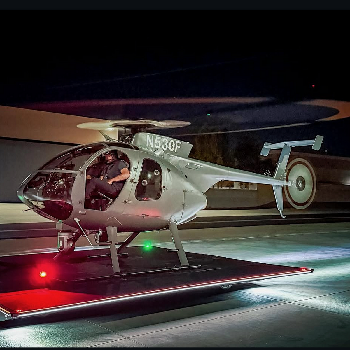 A pilot sits in a light helicopter parked on a platform illuminated by red and white Up-and-Down Stair Lighting LED Channel ~ Model Niza Duo along the edges.