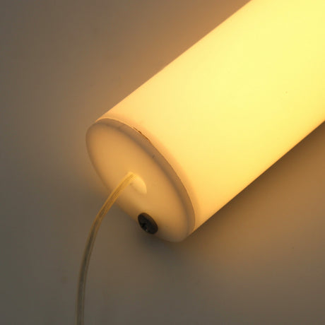 A close-up of the 1.5" White Surface-mount LED Tube Lighting Fixture (24V) ~ Sierra38 Series, glowing with warm light on a flat surface. Its clear power cord connects seamlessly to the bottom of the lamp.
