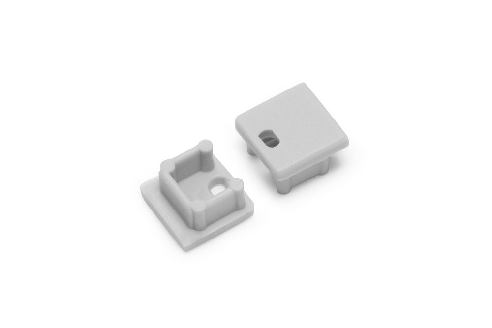 Two small, square, light gray End Caps for Smart10 Profile are shown: one displays its flat top, the other its hollow underside with pegs and a rectangular hole—both designed to fit Smart10 profile lighting fixtures.