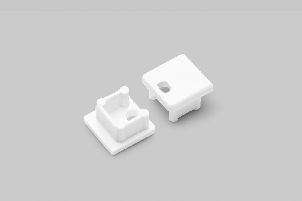 Two End Caps for Smart10 Profile—small, white, square plastic pieces with short pegs and cutout holes—are shown on a light gray background. One cap is flipped to reveal the hollow underside.